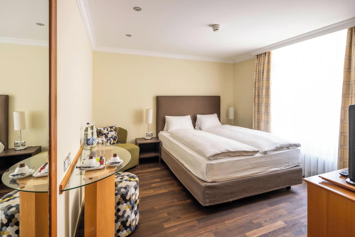 Habitació d'hotel amb un llit, una taula de treball, una cadira, una taula de vidre i una televisió.