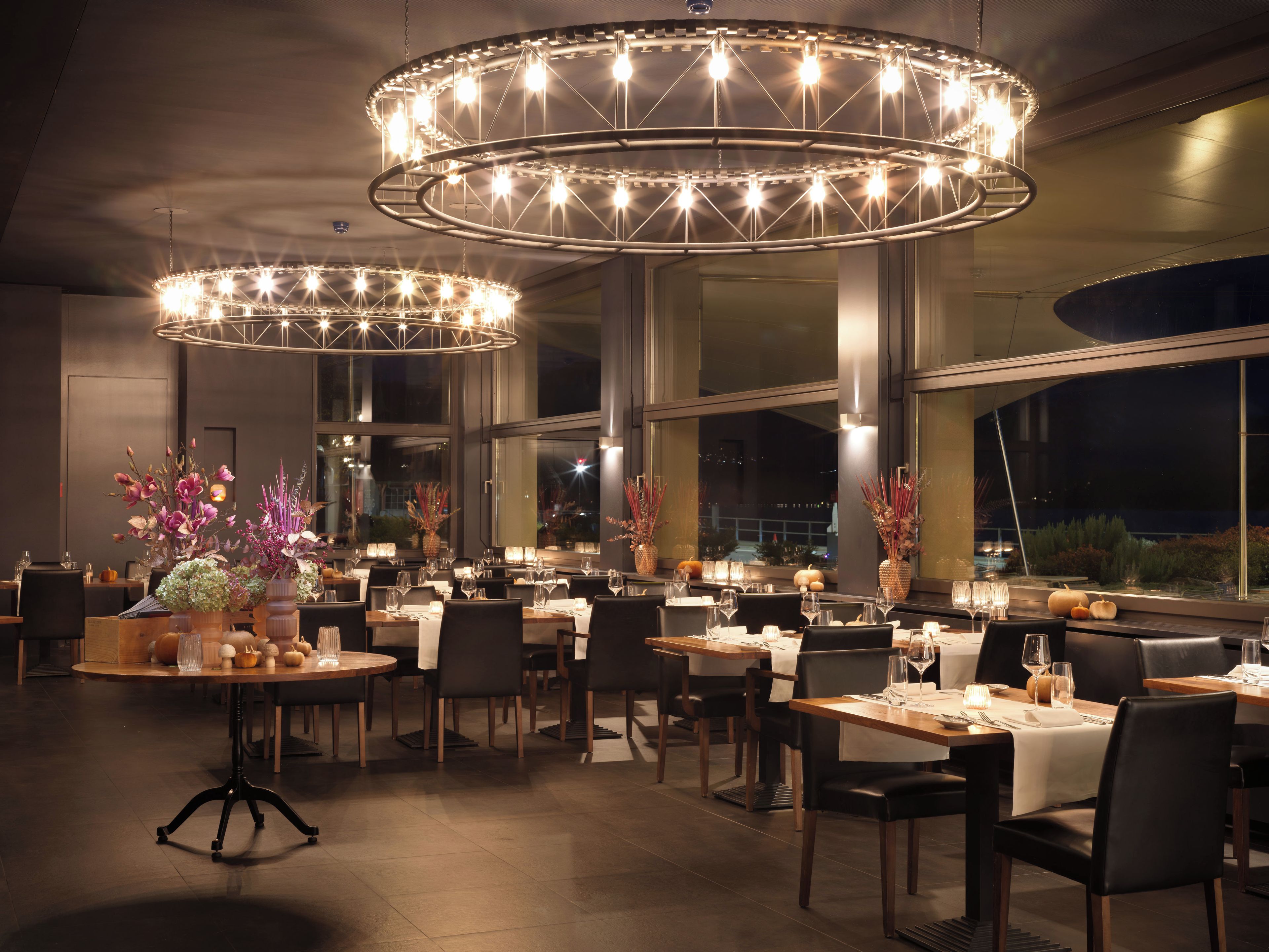 Ein Restaurant mit mehreren Speisetischen, Stühlen und großen, runden Kronleuchtern.