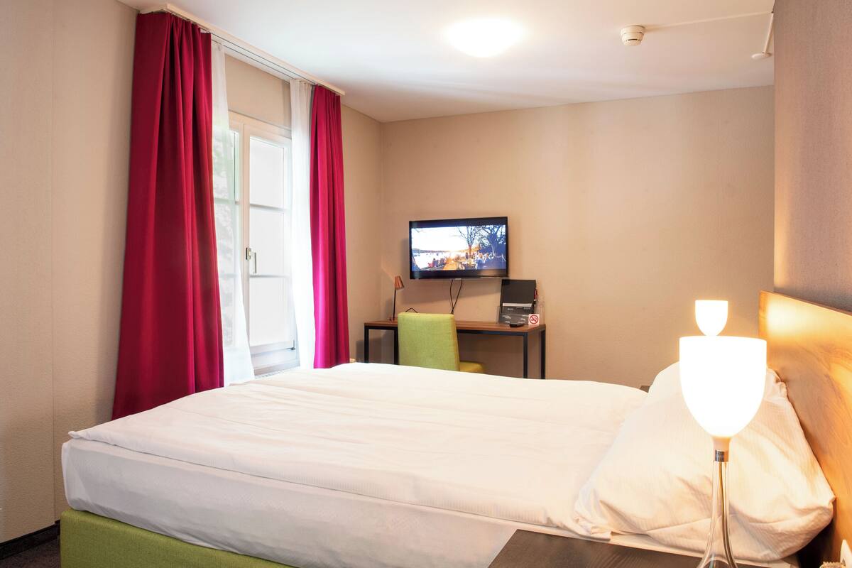 A hotel room with a bed, a desk with a computer, a television, and a lamp.