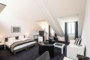 A modern hotel room with a bed, two armchairs, a coffee table, a desk, and a TV. - Hotel Seeburg (Lucerne)