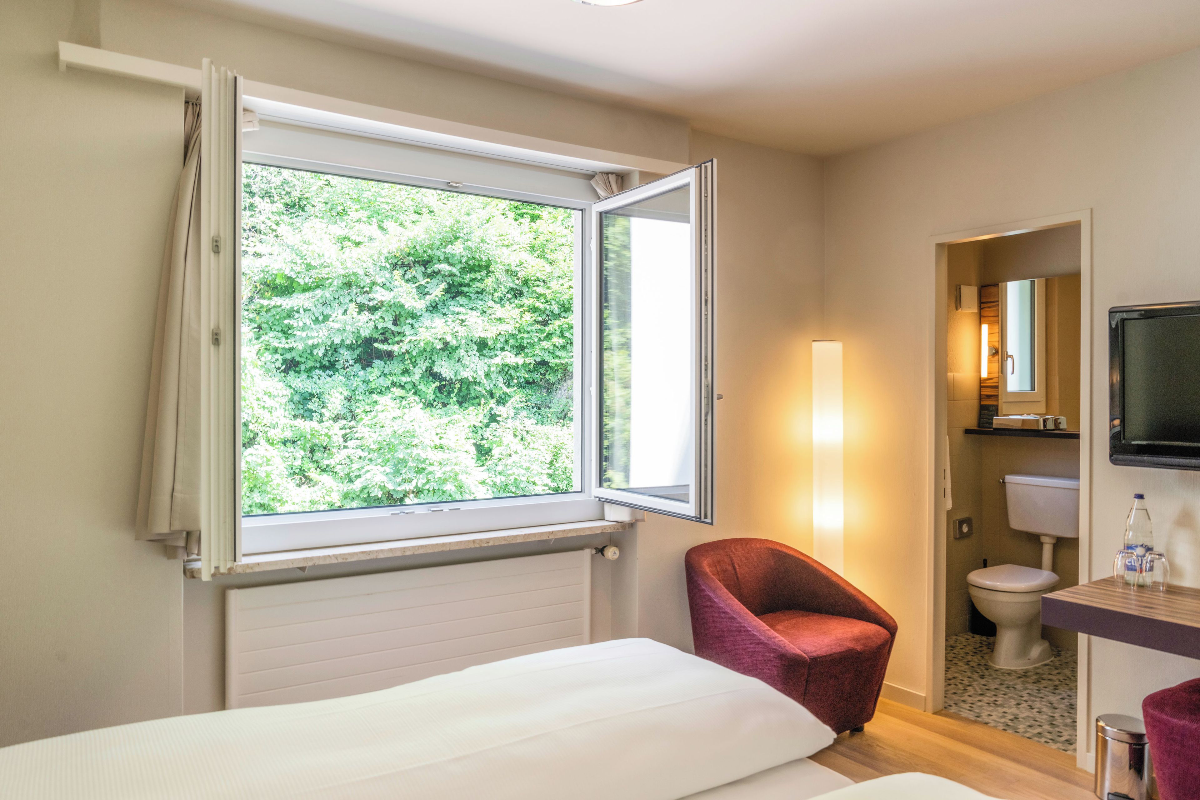 Ein Hotelzimmer mit Bett, Stuhl, Fernseher und einem Fenster mit Vorhängen.