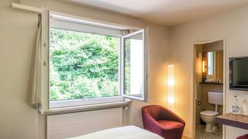 Ein Hotelzimmer mit Bett, Stuhl, Fernseher und einem Fenster mit Vorhängen.