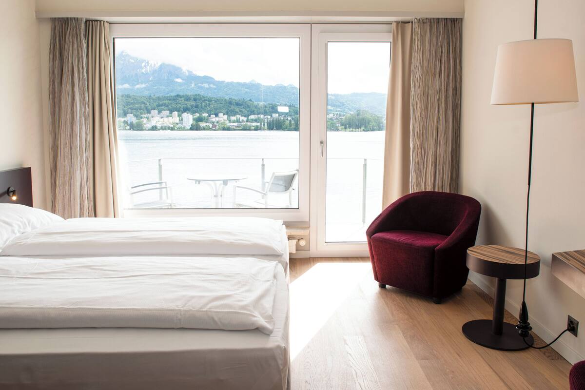 A hotel room with a bed, a red armchair, a small table, and a lamp.