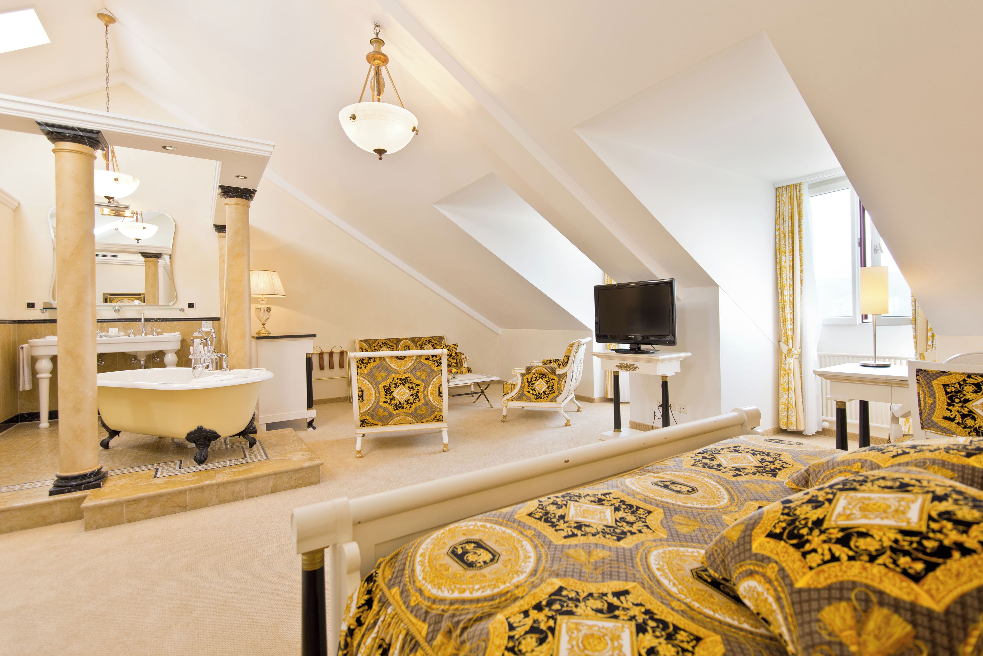 Ein Zimmer mit hohen Decken, einem großen Bett, einer Badewanne, einem Fernseher und einer Essecke.