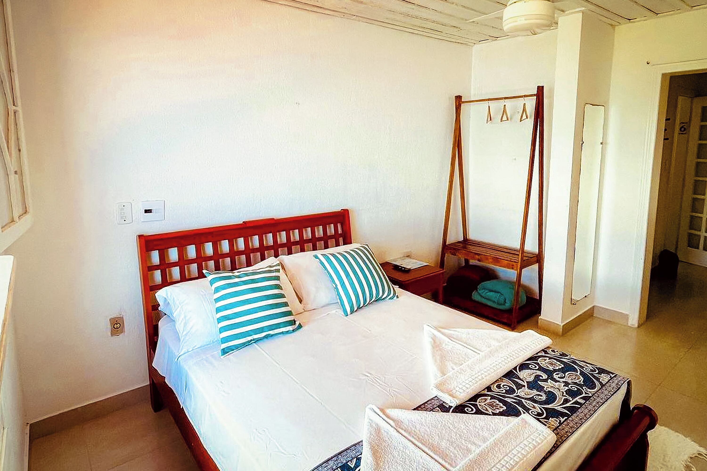 Une chambre à coucher avec un lit en bois, du linge de lit blanc et une table de chevet en bois avec une lampe.