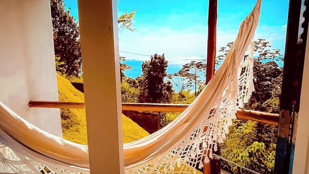 Una hamaca atada entre dos ventanas, con vistas a un paisaje pintoresco con árboles y un cielo despejado.