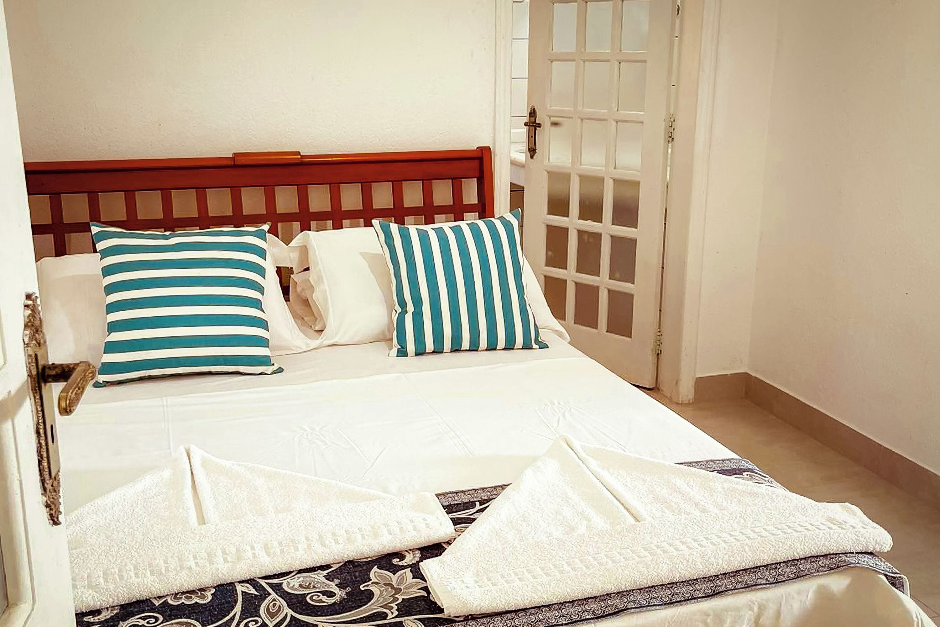 A neatly made bed with striped pillows, a patterned bedspread, and two folded towels.