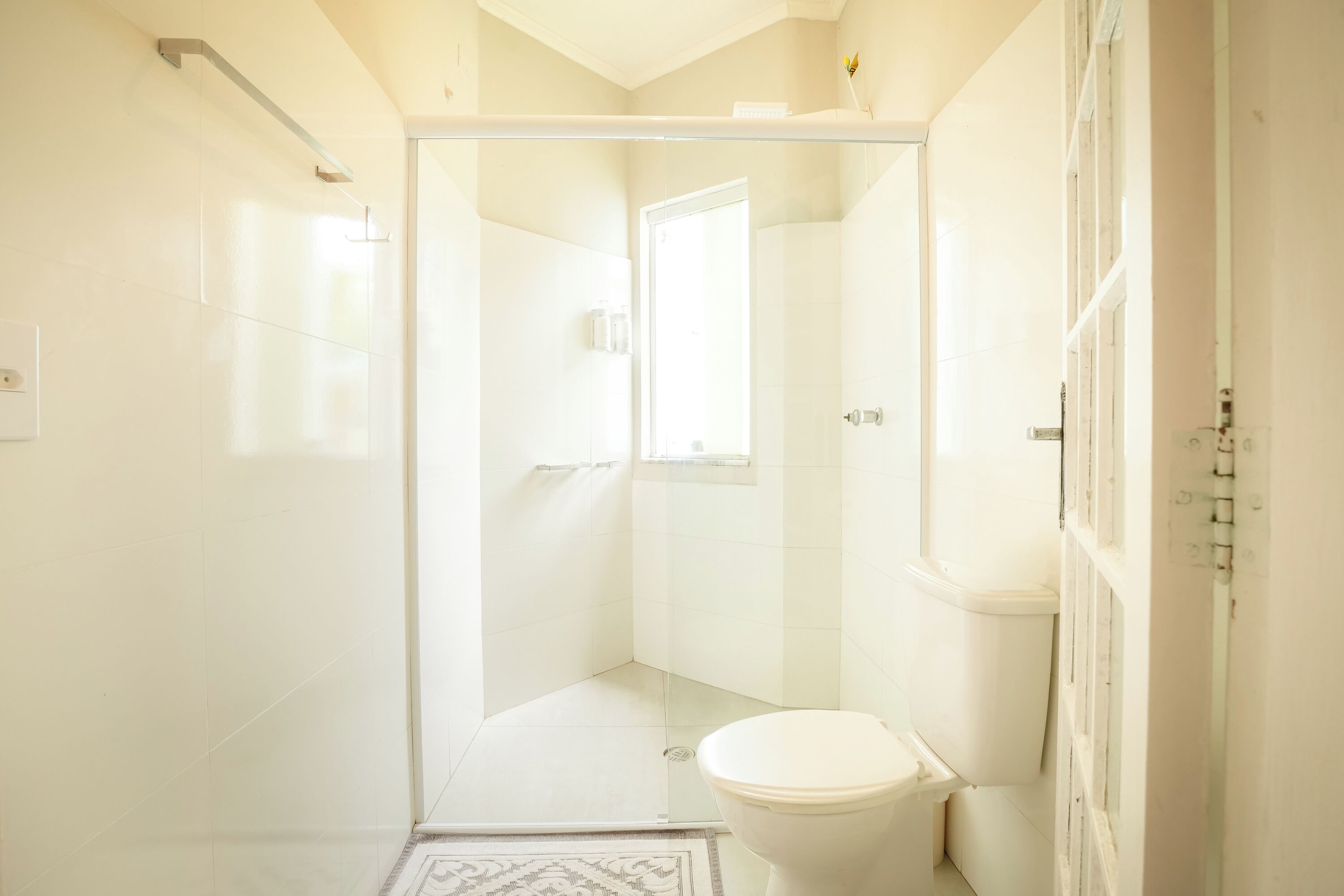Un baño moderno con cabina de ducha de vidrio, inodoro y una ventana pequeña.