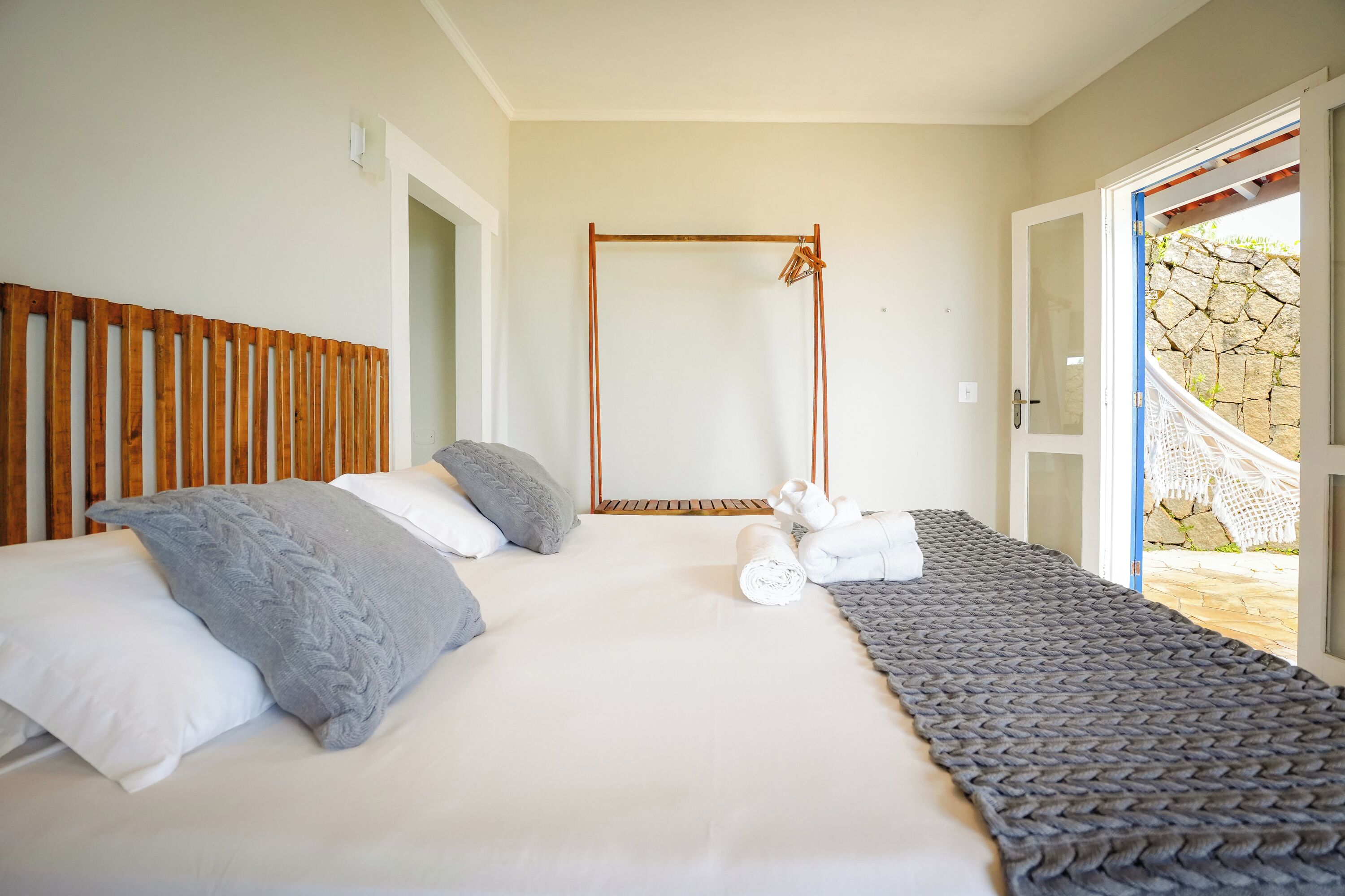 Une chambre à coucher avec un lit, des oreillers, une tête de lit en bois, un porte-serviettes et une vue sur un mur en pierre et un espace extérieur.