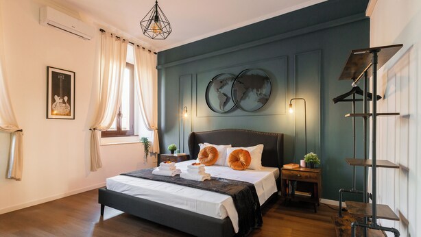 A bedroom with a large bed, a wooden floor, a hanging light fixture, and a world map on the wall. - Pettinari Apartment (Roma)