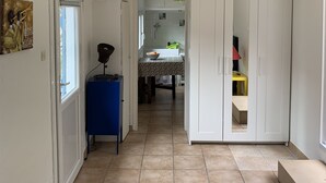 Een smalle gang met een betegelde vloer, die leidt naar een keuken met een raam en een spoelbak.
