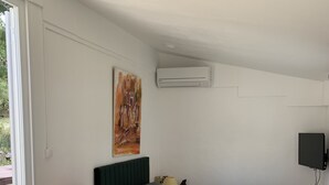 Een slaapkamer met een bed, een rode lamp, een schilderij, een airconditioner en een televisie.