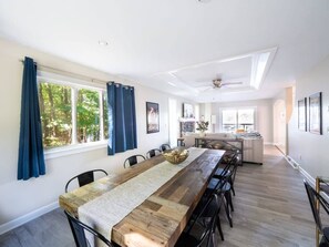 A spacious dining area with a long wooden table, blue curtains, and a view of the outdoors. - Leicester Lake Front Home, Come Relax! (Leicester)