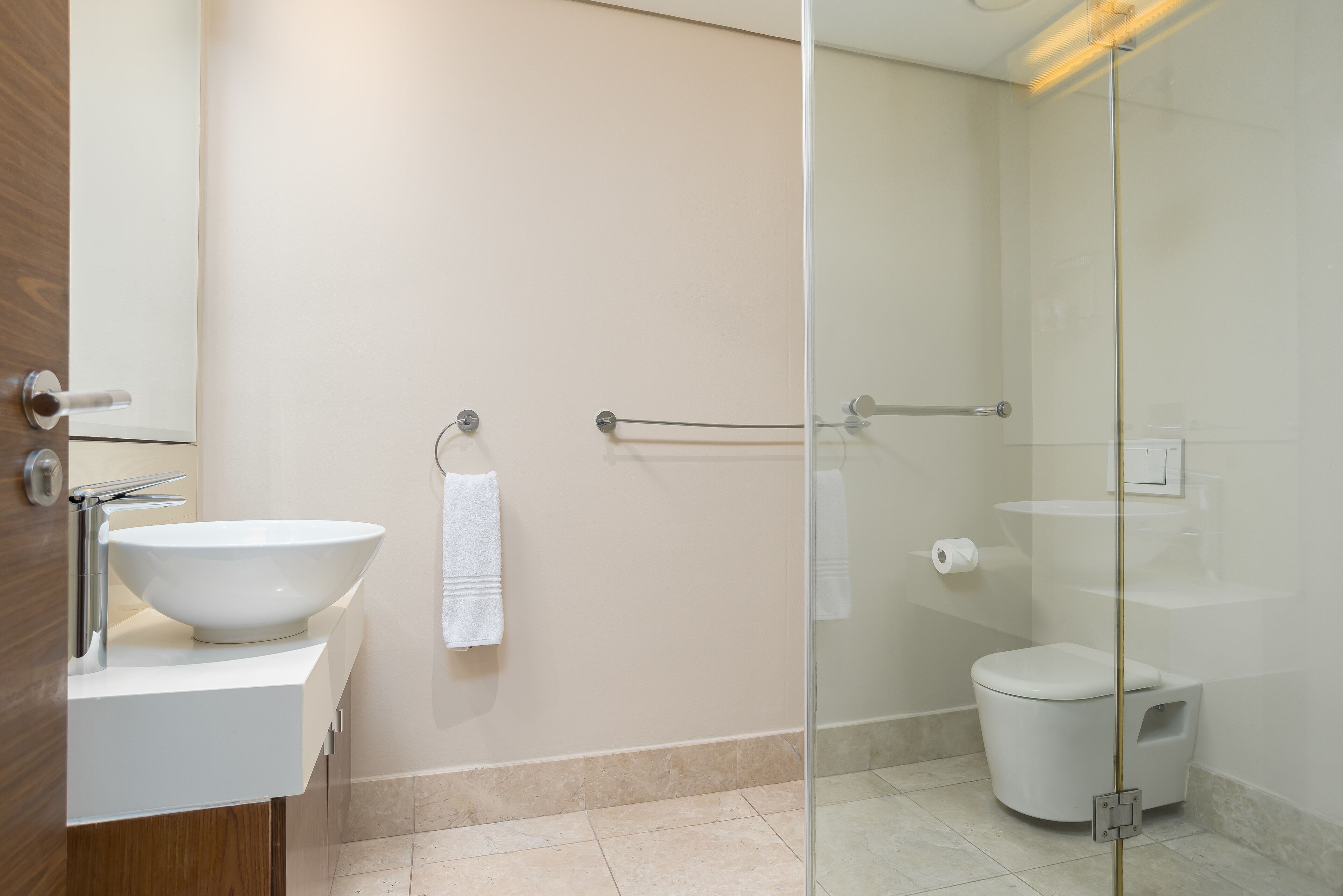 Un baño moderno con un lavamanos grande de color blanco, cabina de ducha de vidrio y un inodoro.