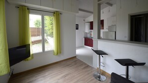 Una cocina moderna con armarios blancos, una zona de comedor con dos taburetes de bar y un televisor montado en la pared.