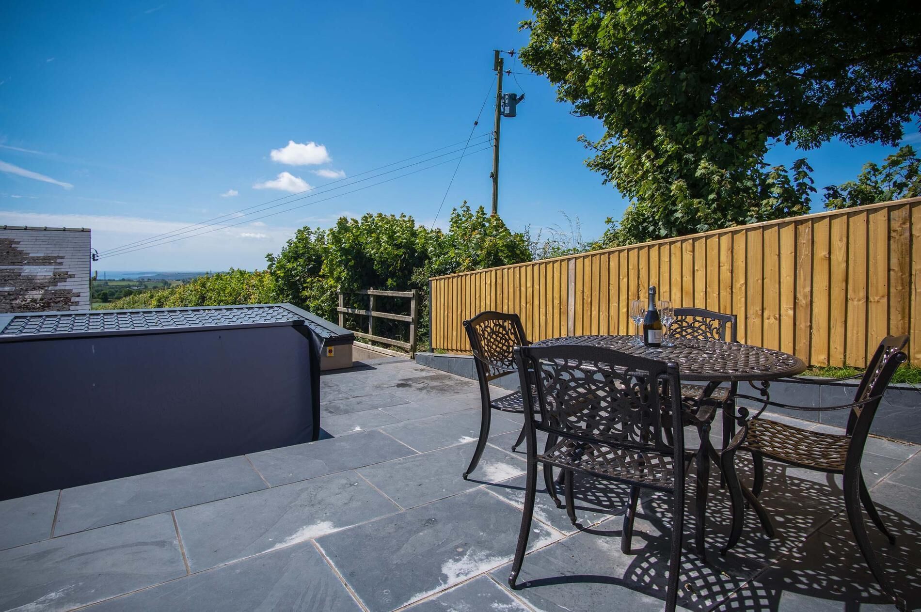 Een terras buiten met een stenen vloer, een houten hek en een tafel met stoelen.