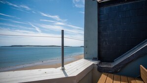 Un balcón con vista al mar, una terraza de madera y una pared negra.