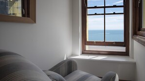 Ein Eckzimmer mit Meerblick, einer weißen Wand und einem Streifenstuhl.