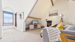 A cozy living room with a television, sofa, and a view of the sea through a window.