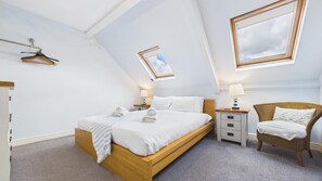 A bedroom with a wooden bed, a nightstand, a chair, and a window with a view of the sky. - The Nest - 1 Bedroom Apartment - Tenby (Tenby)