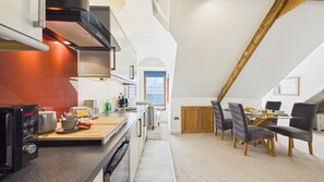 Une cuisine moderne dotée d’un four encastré, un coin repas avec une table en verre et une vue sur la mer par une fen être.