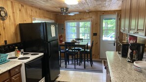 A wooden cabin kitchen with a black refrigerator, white stove, and granite countertops. - Eagle Bay Cottage with Lake Rights (Eagle Bay)