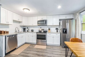 A compact kitchen with white cabinets, a microwave, a stove, a dishwasher, and a refrigerator. - Cozy & Modern w/Hot Tub, Fire Pit, Grill & Pond (Berkeley Springs)