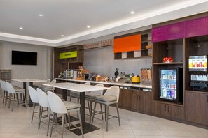 A modern cafe with a counter, seating area, and a refrigerator stocked with beverages.