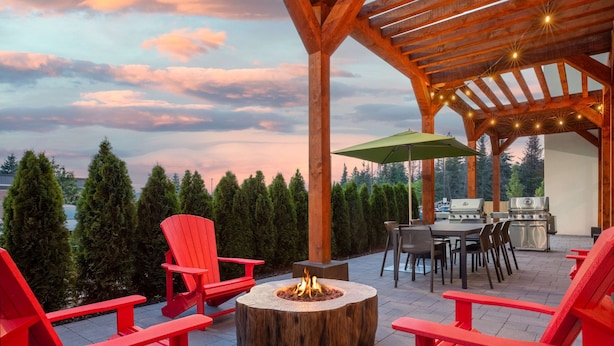 A covered patio with red Adirondack chairs, a fire pit, and a grill area.