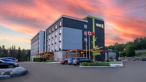 A modern hotel with a prominent "HOME2" sign, a parking lot, and a scenic sunset backdrop.