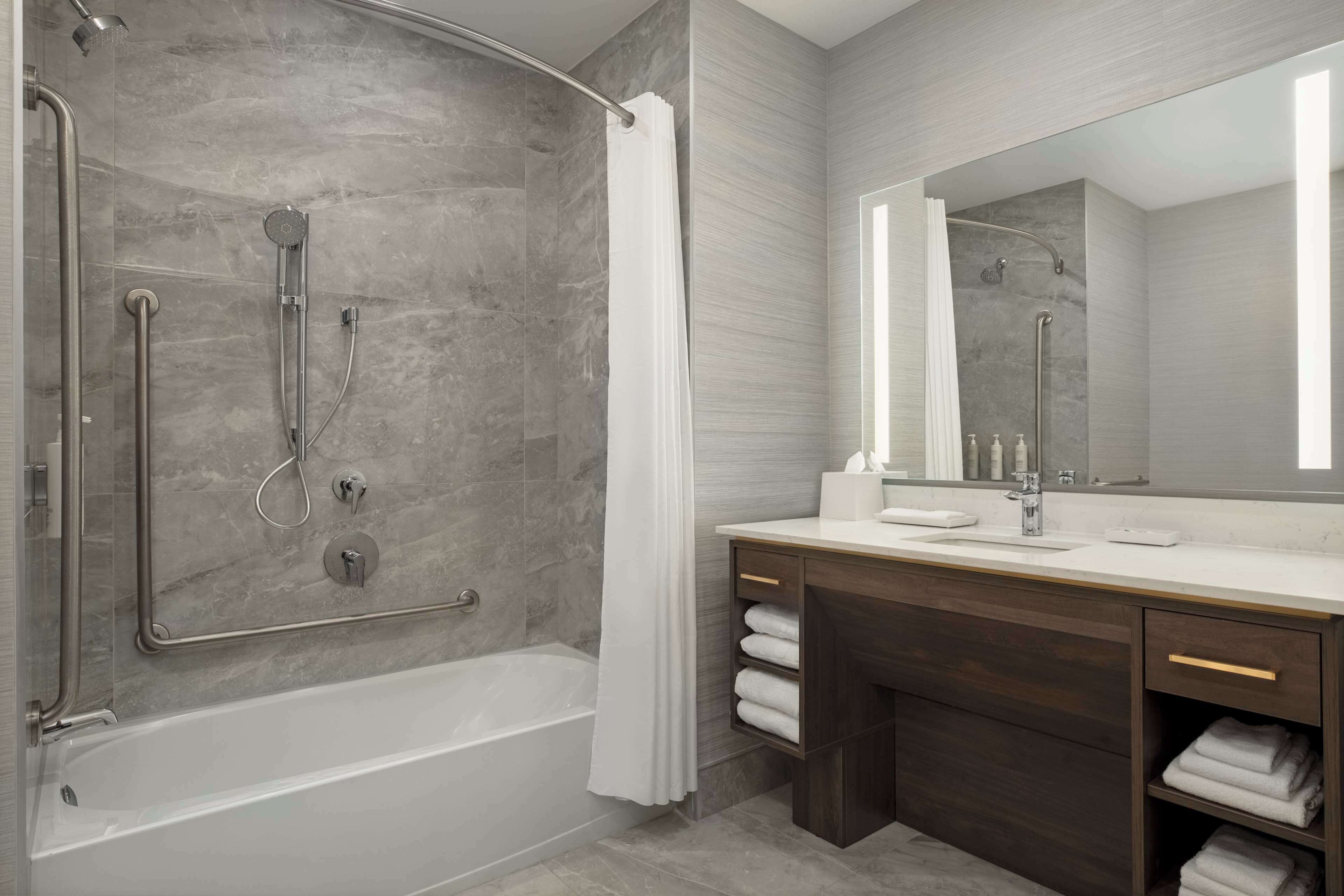 A modern bathroom with a walk-in shower, a bathtub, a vanity with a mirror, and a towel rack.