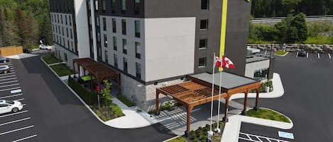 Un hotel moderno con un llamativo letrero de 'Home 2 Suites by Hilton', un área de estar al aire libre cubierta y un estacionamiento con espacios delimitados.