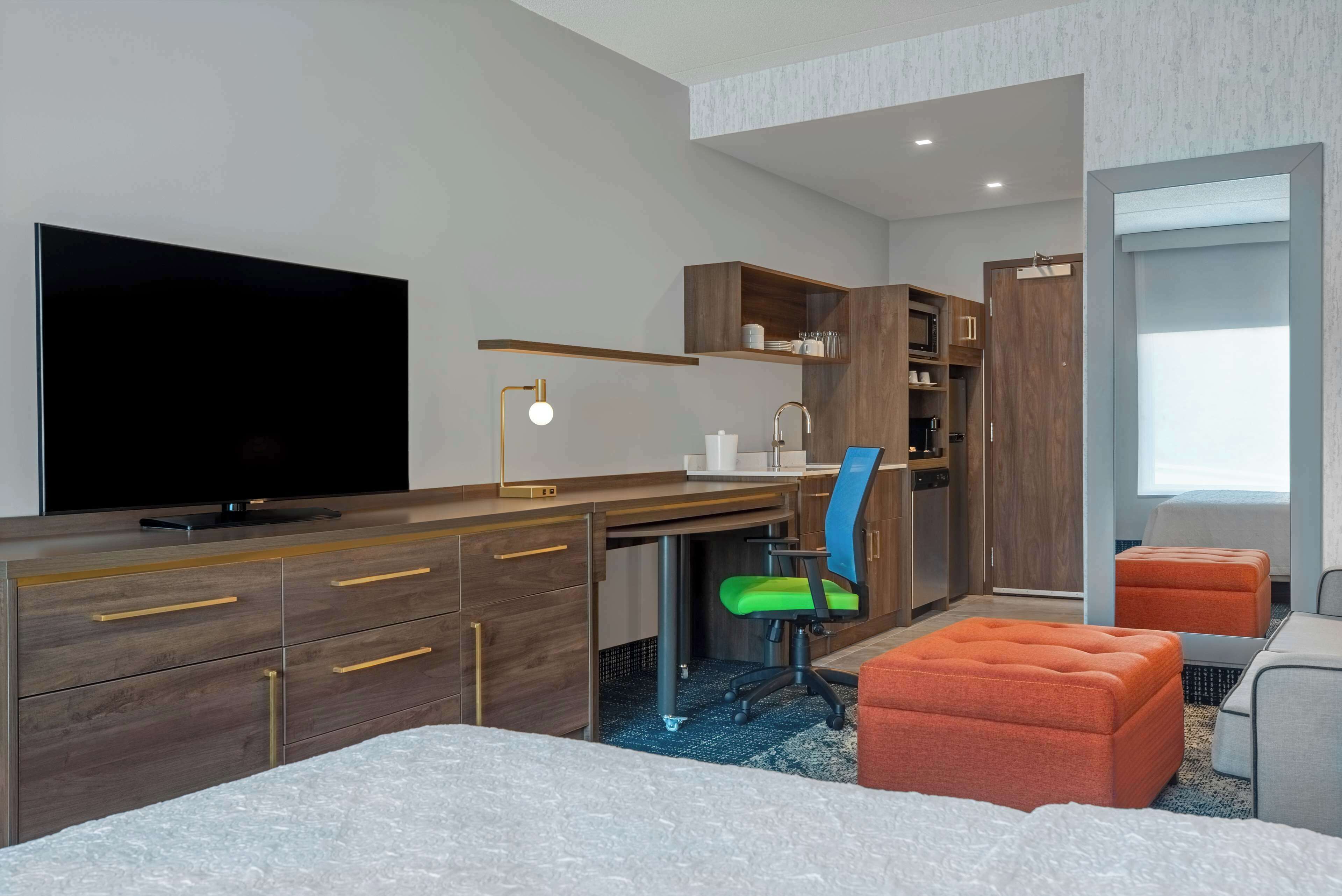 A modern hotel room with a large bed, a desk with a computer, a television, and a wardrobe.