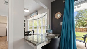 A kitchen with a granite countertop, black chairs, and a window with blinds.