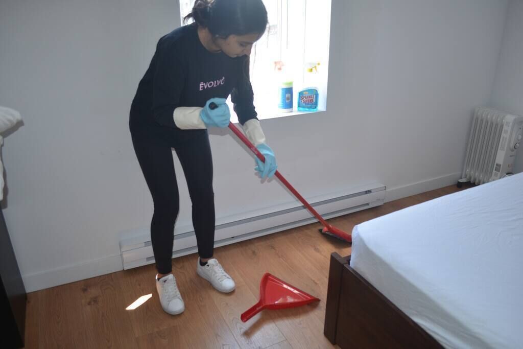 A person cleaning a wooden floor with a red mop and a red dust pan.