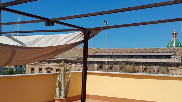 Eine Terrasse mit Metallgestell, einem Blumentopf mit einem Kaktus und einem Gebäude mit grüner Kuppel im Hintergrund.