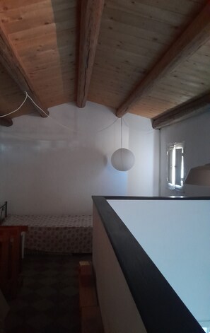 A room with a wooden ceiling, a hanging light fixture, a window with blinds, and a bed with a patterned bedspread.