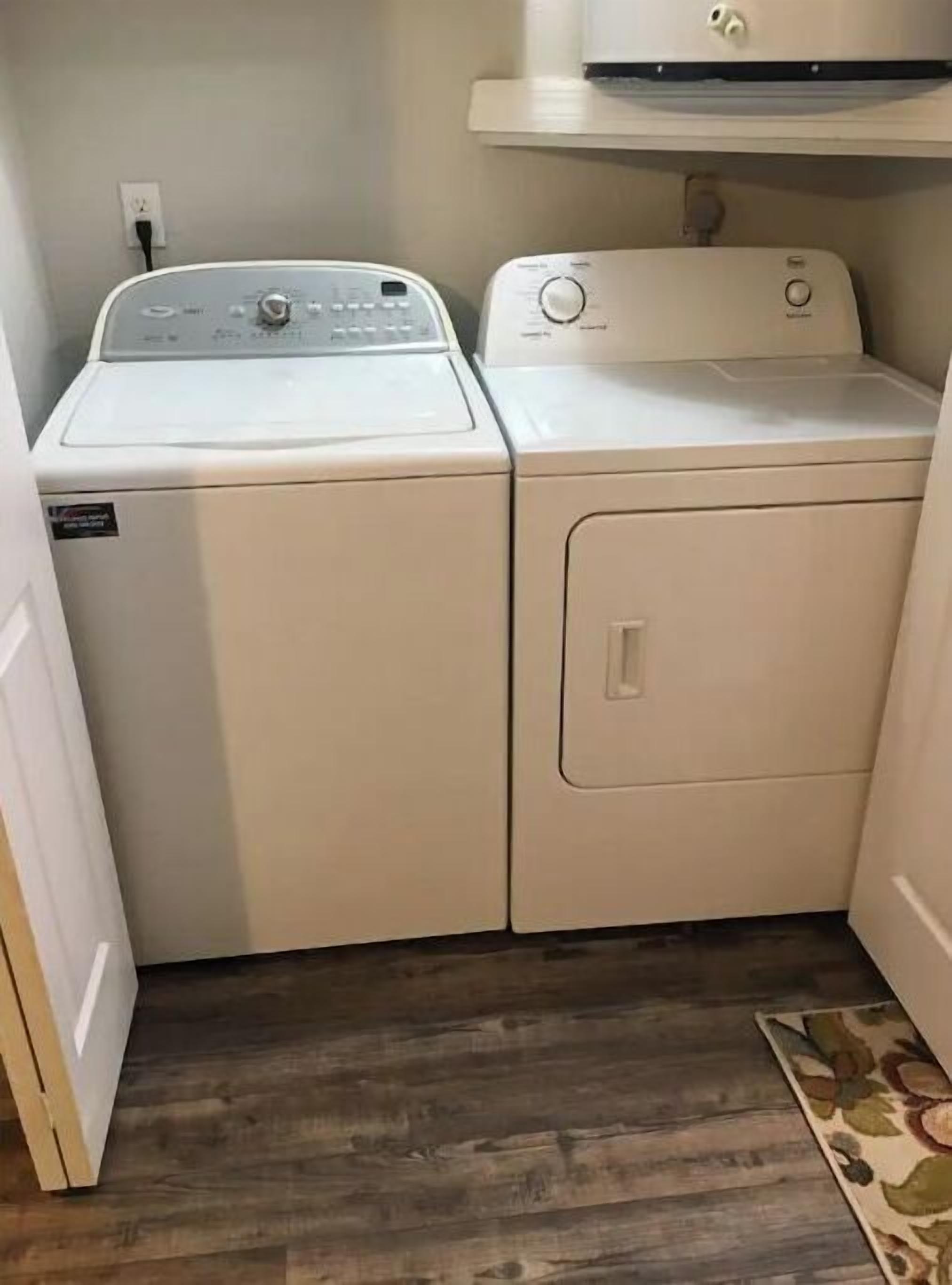 Une buanderie équipée de deux machines à laver et deux sèche-linge superposés, avec un plancher en bois et un petit tapis.