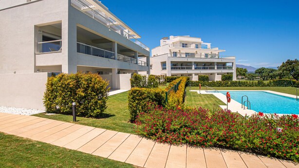 Un bâtiment moderne à deux étages, doté d’une piscine, entouré de jardins bien entretenus et surplombé d’un ciel bleu azur.