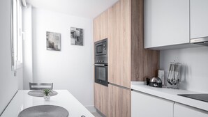 Une cuisine moderne avec un plan de travail blanc, un pare-feu en panneaux de bois et des appareils électroménagers intégrés.