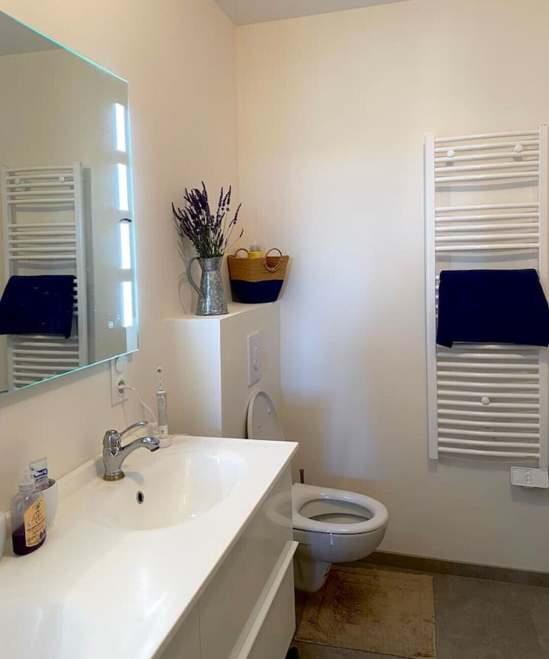 Un baño con lavamanos blanco, espejo, inodoro y toallero.