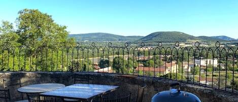 An outdoor patio with a table and chairs, a barbecue grill, and a view of distant hills.