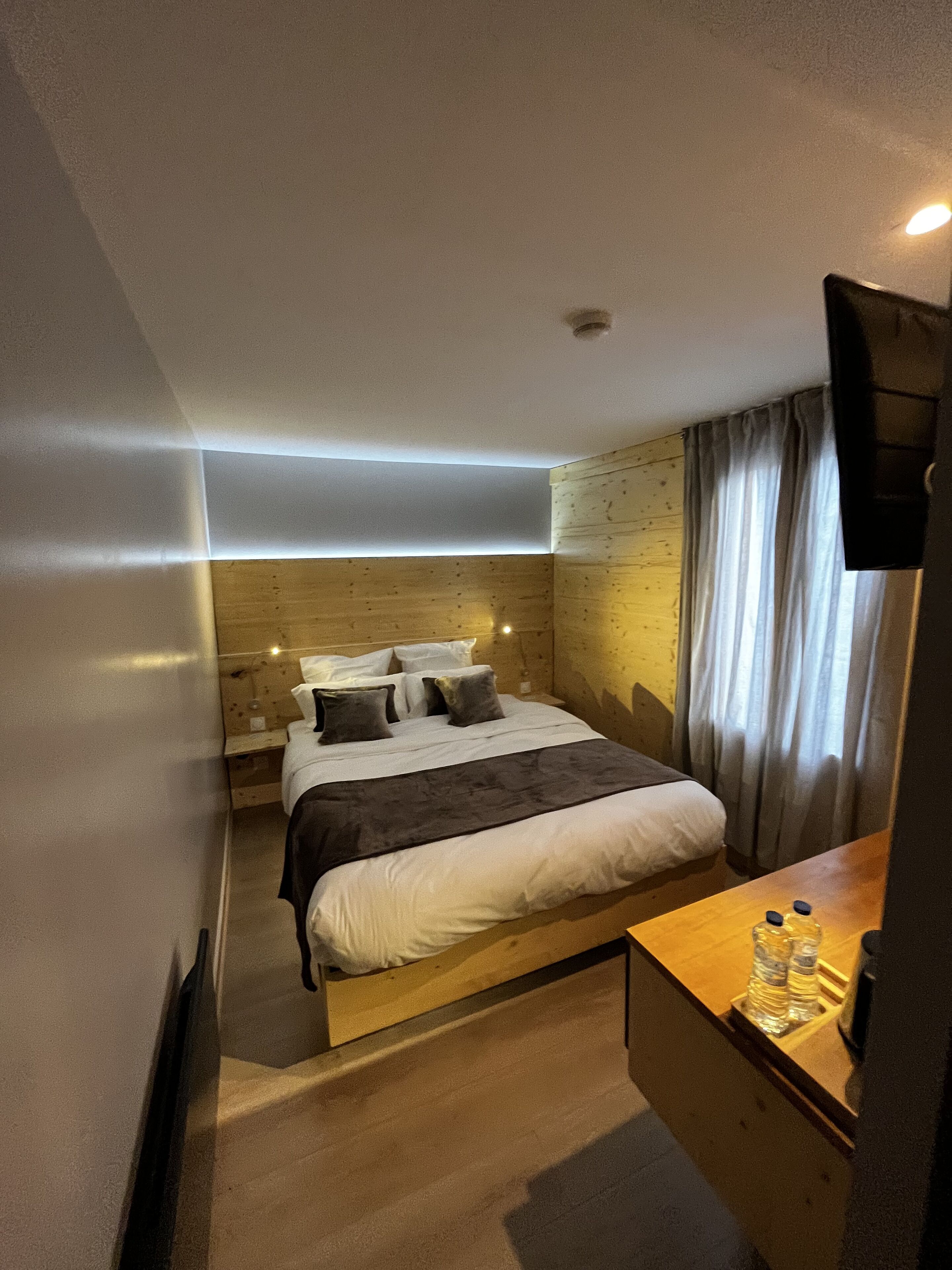 A modern hotel room with a wooden bed, bedside tables, and a flat-screen TV.