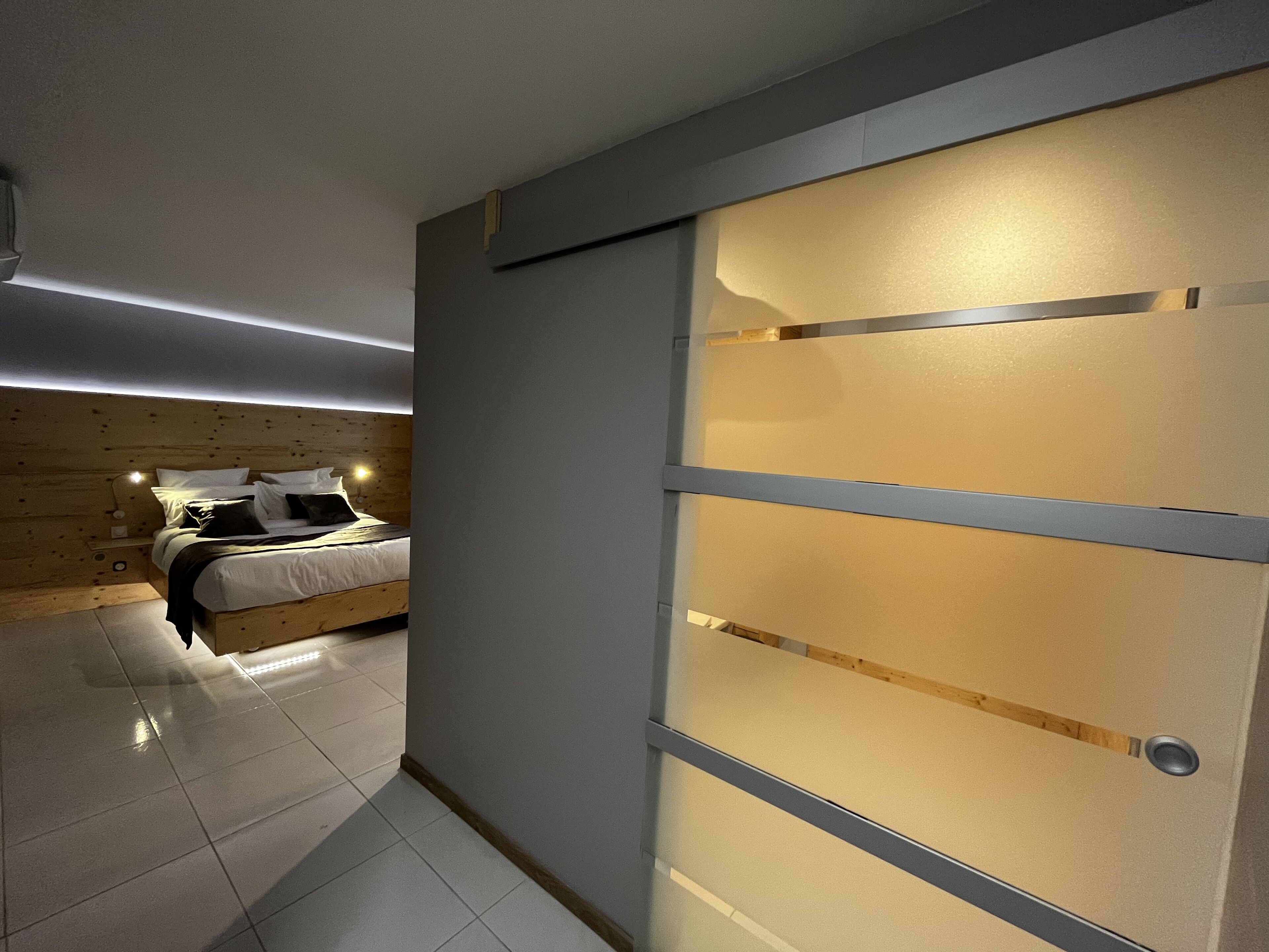 A modern bedroom with a bed, a wooden headboard, and a sliding door with frosted glass panels.