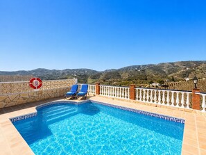 A swimming pool with a view of hills, two blue lounge chairs, and a no swimming sign.