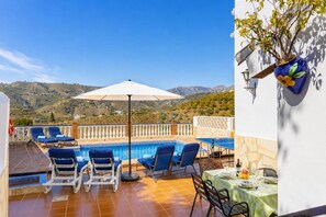 Une terrasse avec une piscine, des chaises longues bleues, une table à manger et une vue sur les collines.