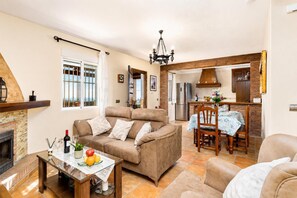 A living room with a sofa, a dining table with chairs, a fireplace, and a kitchen area with a refrigerator and stove.