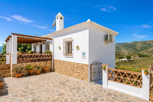 A white building with a stone-paved patio, a covered seating area, and a view of the countryside.