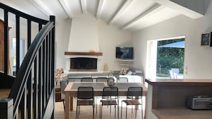A modern kitchen with a central island, a dining area with chairs, and a staircase with black railings. - Villa TOUT CONFORT - Les pieds dans l'eau - 3 minutes walk from the sea (L'Épine)