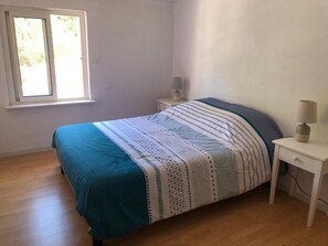 A bedroom with a bed, a nightstand, a lamp, and a window. - Fully Equipped Villa—direct access to the beach, just a 3-minute walk away, and close to shops (L'Épine)